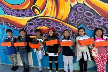 a group of kids holding shoeboxes in front of a colorful mural