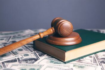 a wooden gavel laying on a green book surrounded by money