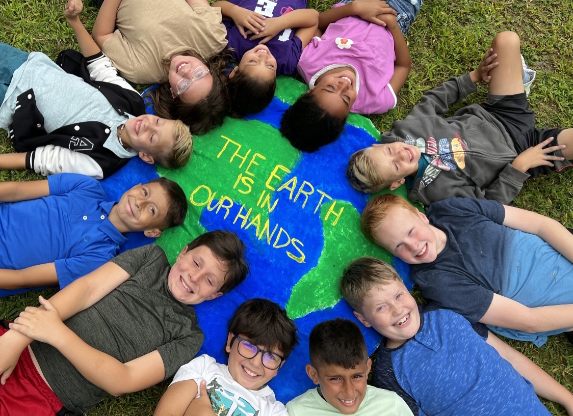 children laying on the ground by a painting that says "the earth is in our hands"