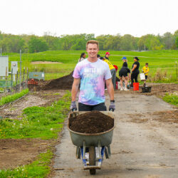 a man rolling a wheelbarrow in a field where others are gaardening