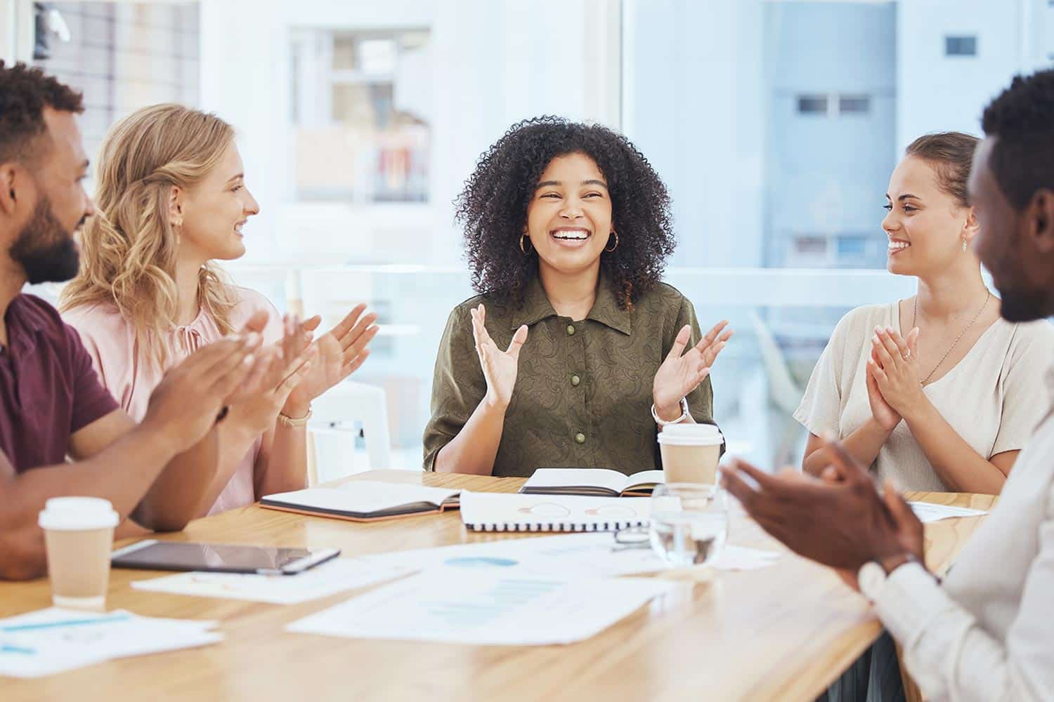people smiling and clapping around a meeting table