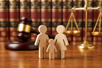 Legal scales and gavel in background, wooden figures of family in foreground